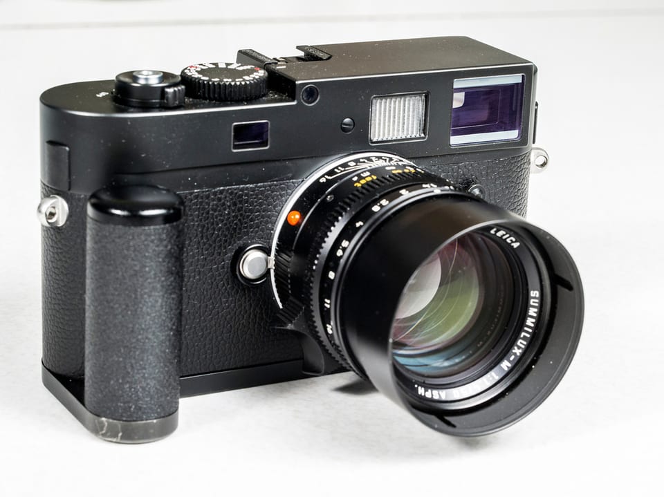 Leica M Monochrom with a 50 mm Summilux and grip, three-quarter view on white